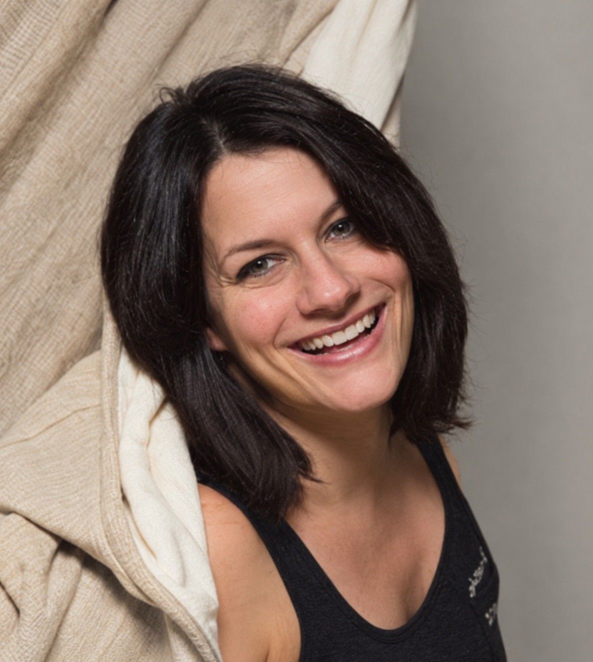 Katja Henschel mit dunklem, schulterlangem Haar lacht in die Kamera, im Hintergrund ein heller Stoff
