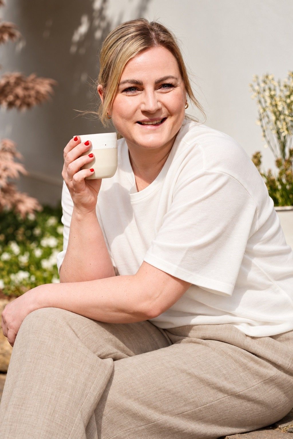 Maike sitzt lächelnd in der Sonne und hält eine Tasse in der Hand